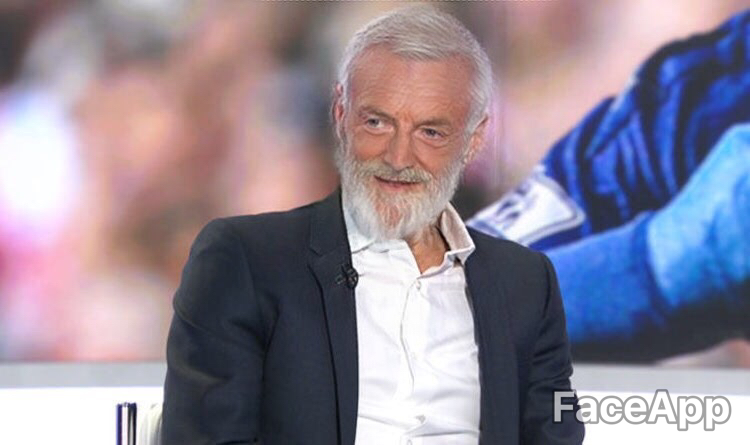 A man with a white beard sitting on a television.