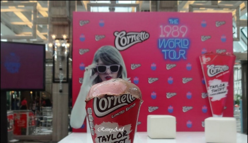 A person holding a cone of ice cream in front of a pink wall.