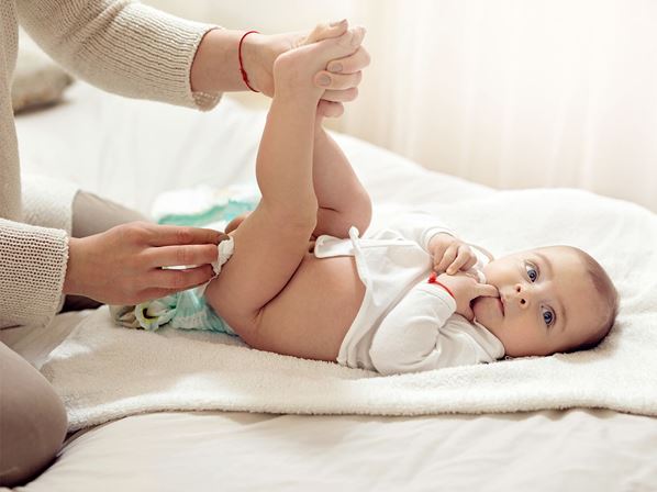 A baby is sitting on a bed with a diaper on it.