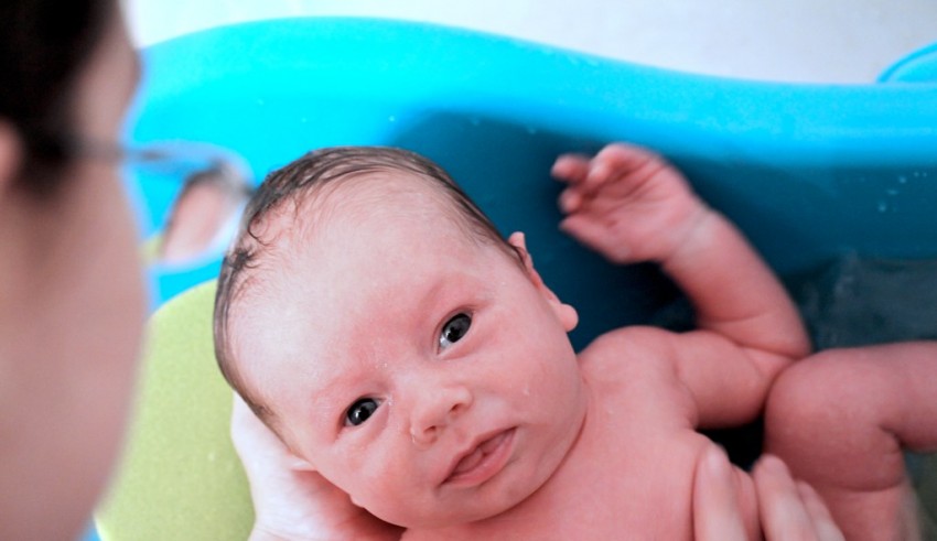 A baby is being bathed in a blue tub.