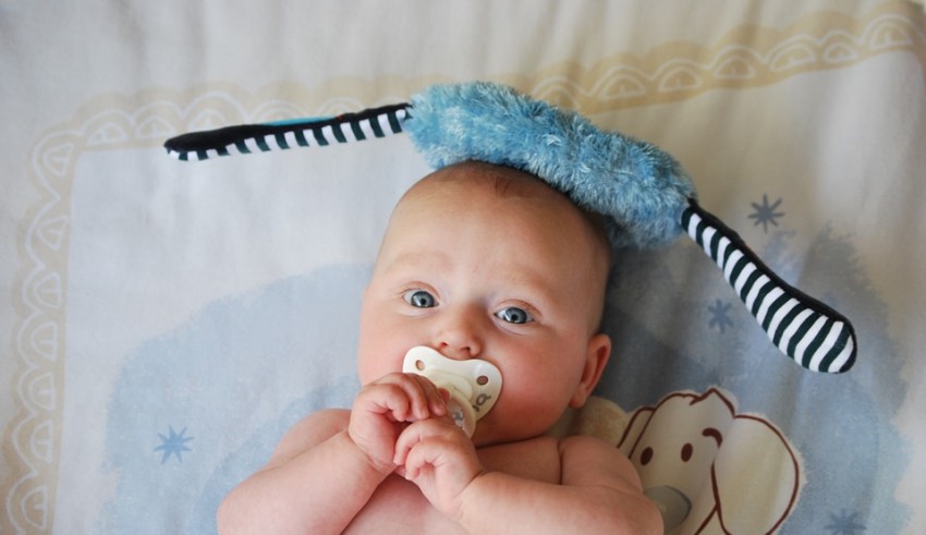 A baby laying on a bed with a pacifier.