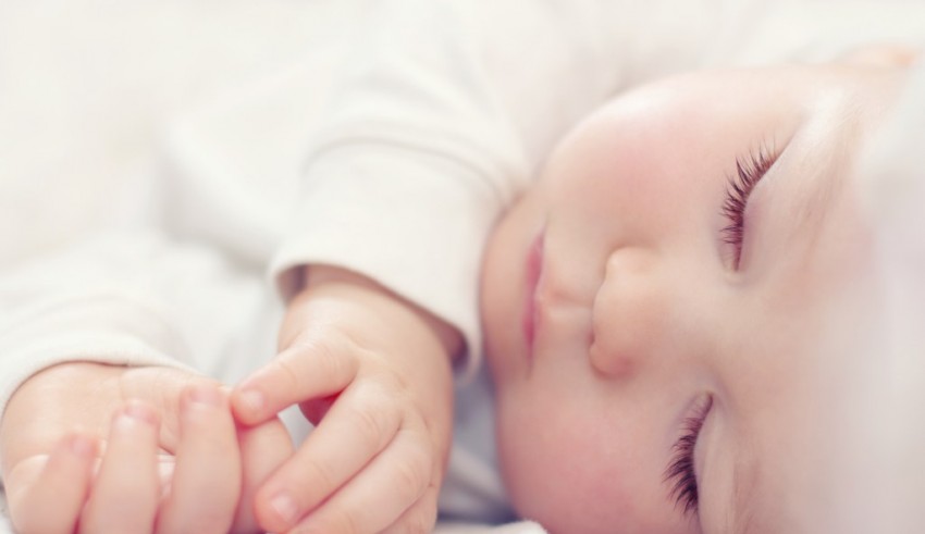 A baby is sleeping on a white bed.