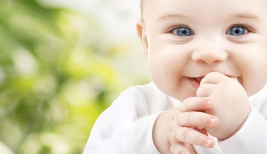 A baby is smiling with his finger on his mouth.