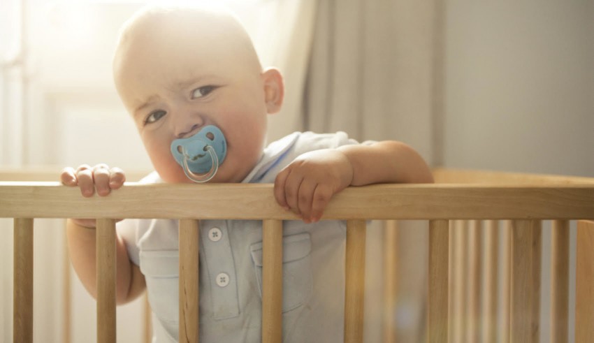 A baby in a crib with a pacifier in his mouth.