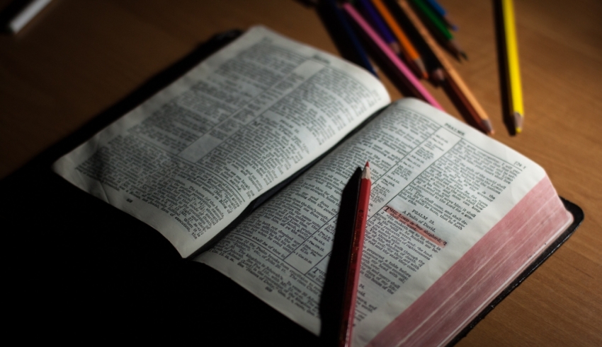An open bible with colored pencils on a wooden table.