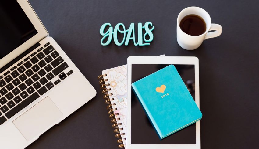 A notebook with the word goals next to a laptop and a cup of coffee.