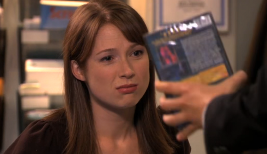 A woman is holding a book in front of a man.