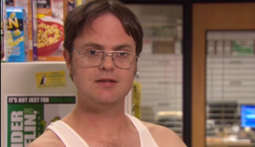 A man in a white tank top standing in front of a refrigerator.
