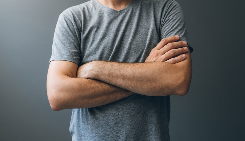 A man with his arms crossed posing against a gray background.