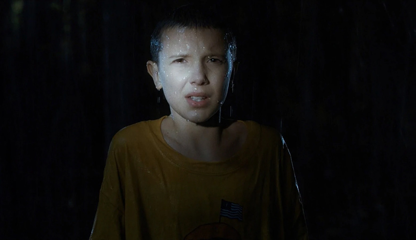 A boy in a yellow shirt is standing in the woods.