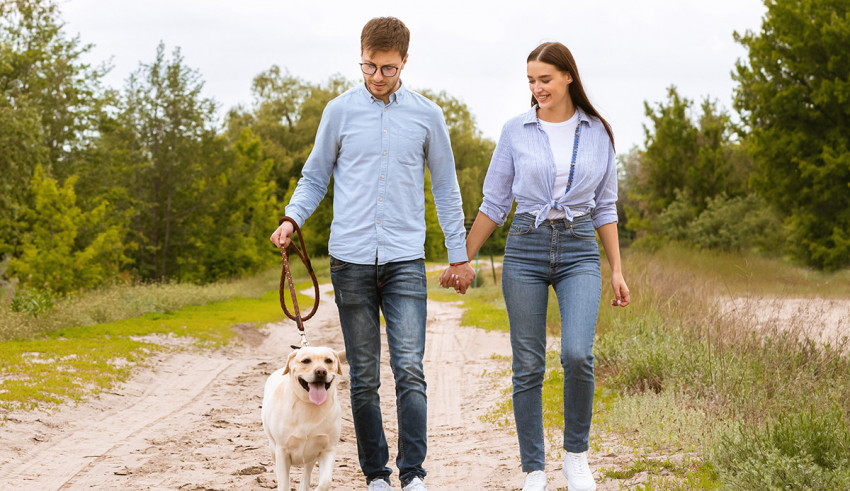 A couple walking their dog on a dirt road.