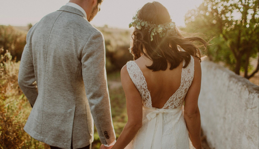 A bride and groom walking through a field at sunset.