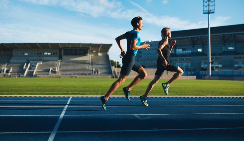 Two men running on a track in a stadium.
