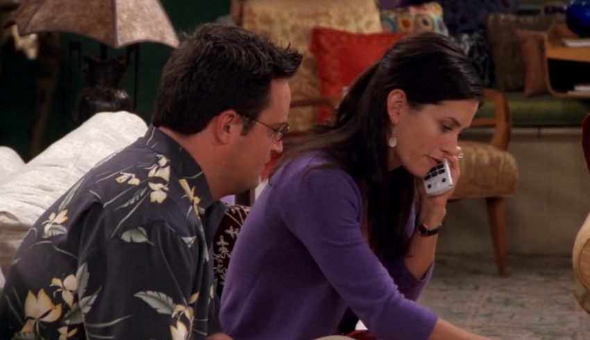 A man and woman sitting on a couch talking on a cell phone.