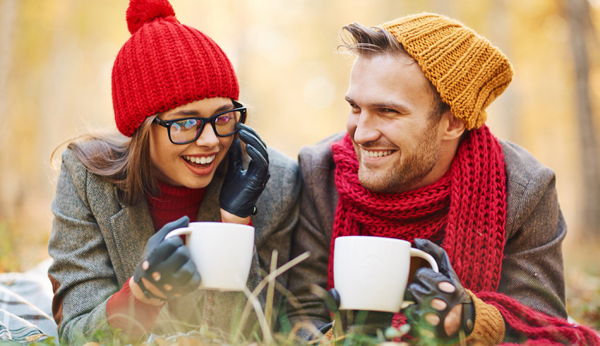 A man and woman holding coffee mugs in the grass.