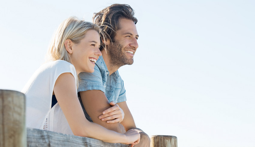 A couple looking at the ocean while leaning on a fence.