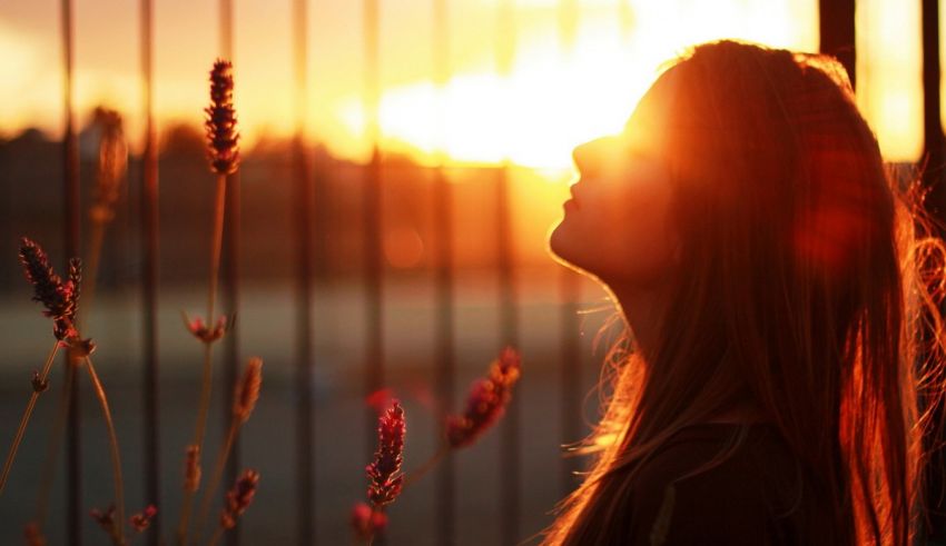 A woman looking at the sun through a fence.