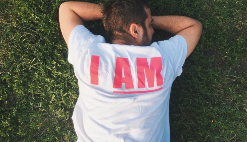 A man laying on the grass wearing a t - shirt that says i am.