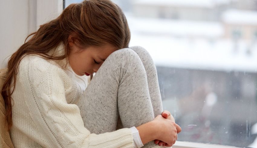 A girl sitting on a window sill with her hands on her knees.