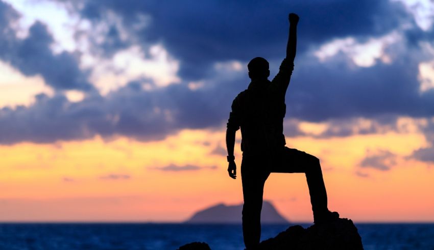 A silhouette of a man standing on top of a rock at sunset.