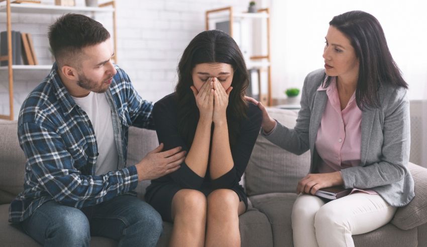 Three people sitting on a couch with a woman covering her face.