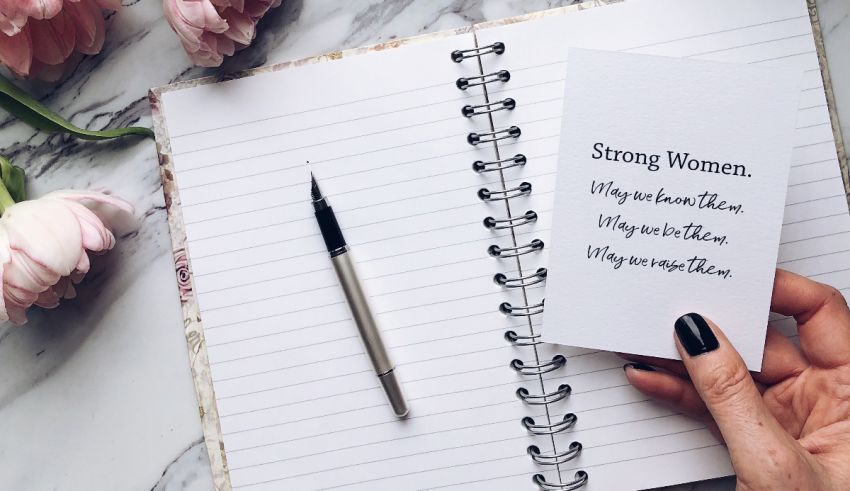 A hand holding a notebook with the words strong women.
