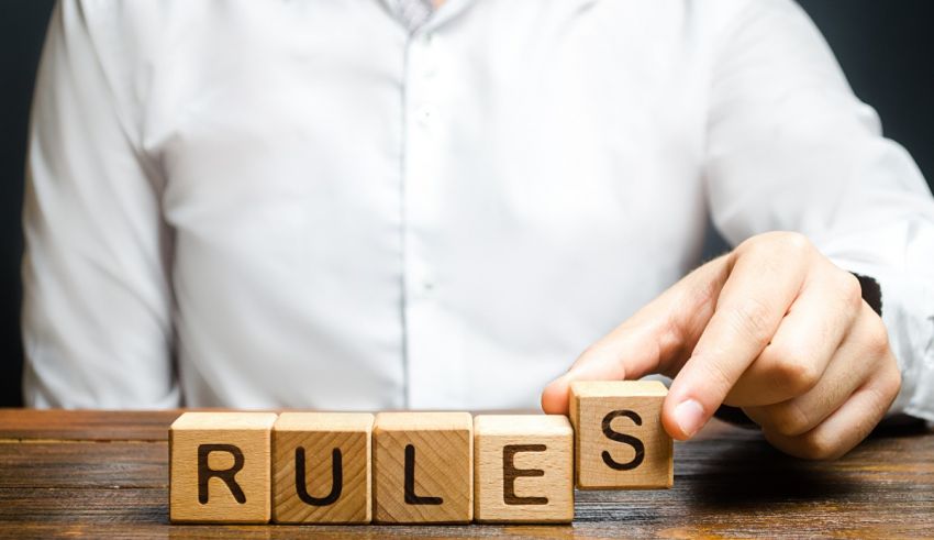 A man is pointing at a wooden block with the word rules written on it.