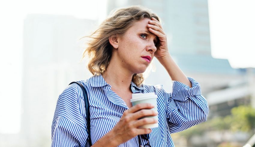 A woman holding a cup of coffee with her hand on her head.