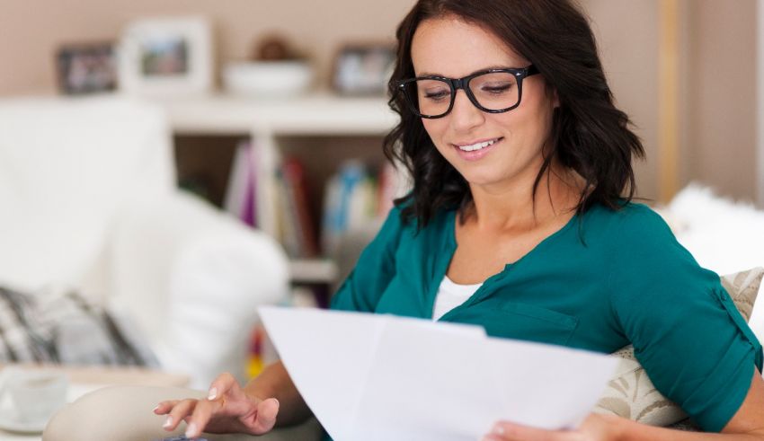 A woman wearing glasses is sitting on a couch and looking at a piece of paper.