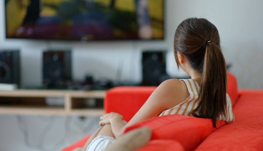 A woman sitting on a red couch watching tv.