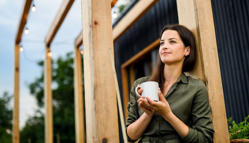 A woman leaning against a wooden fence holding a cup of coffee.