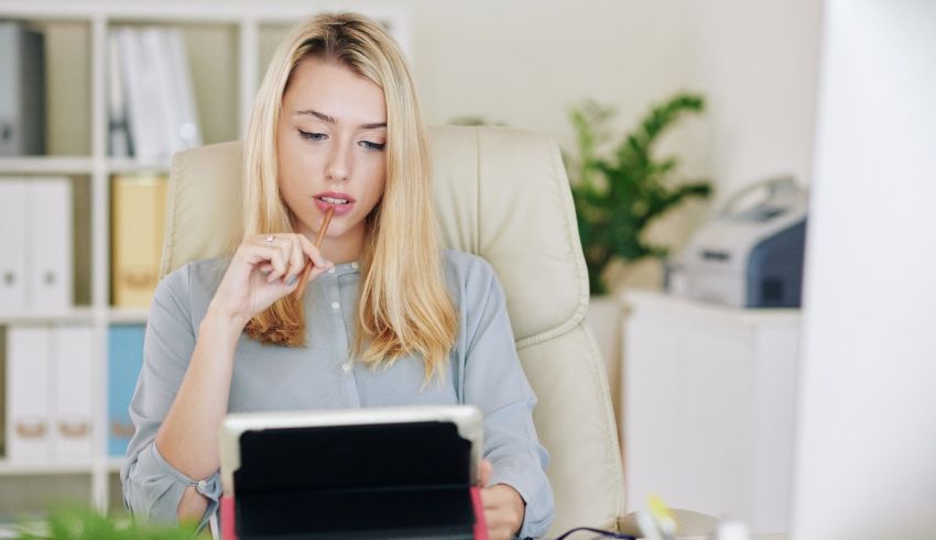 A young woman is sitting at her desk using a tablet computer.