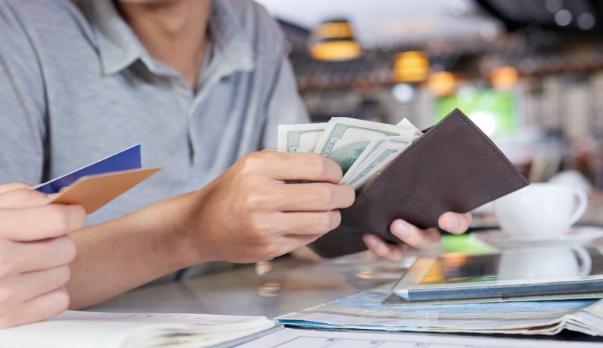 A man is holding a wallet and money while sitting at a table.