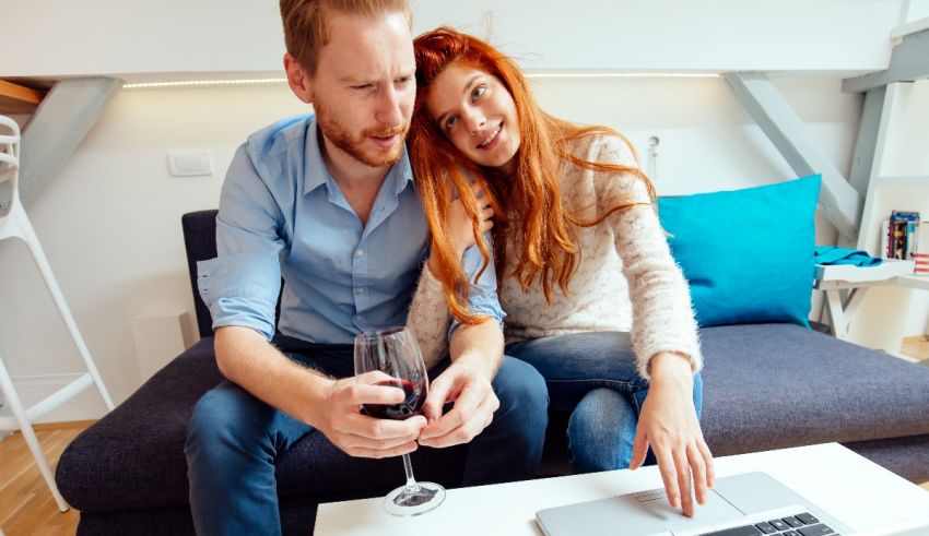 A man and woman sitting on a couch looking at a laptop.