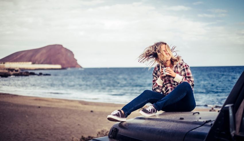 A woman sitting on top of a jeep on the beach.