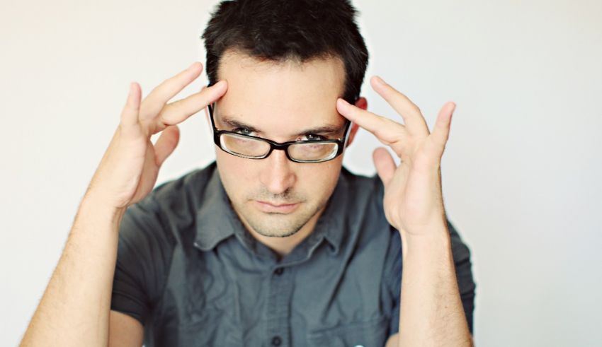 A man with glasses holding his hands to his head.