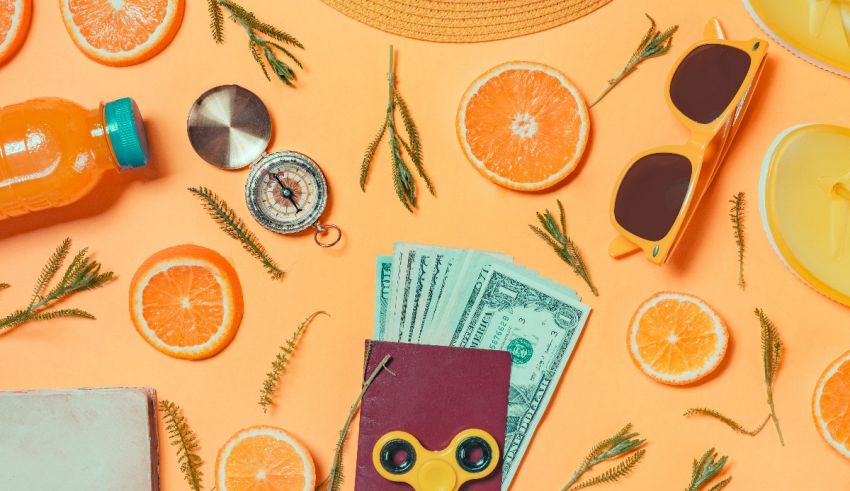 An orange, hat, sunglasses, and a book on a yellow background.