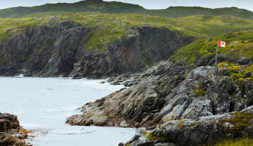 A canadian flag flying over a rocky shore.