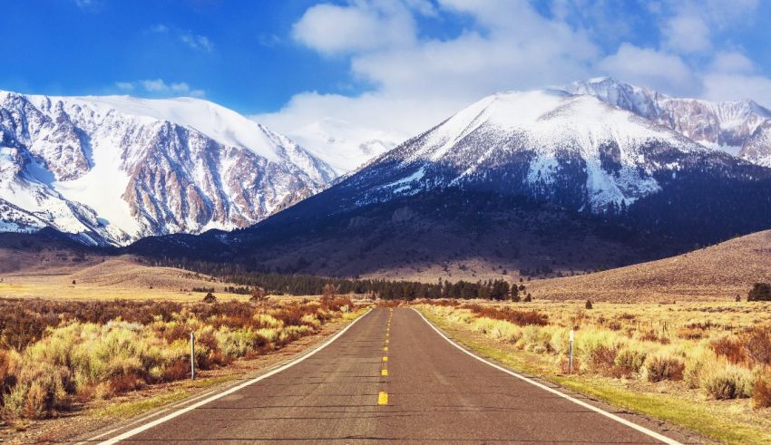 An empty road with snowy mountains in the background.