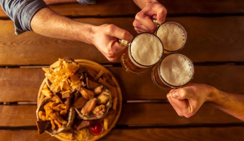 A group of people toasting with beer and chips on a wooden table.
