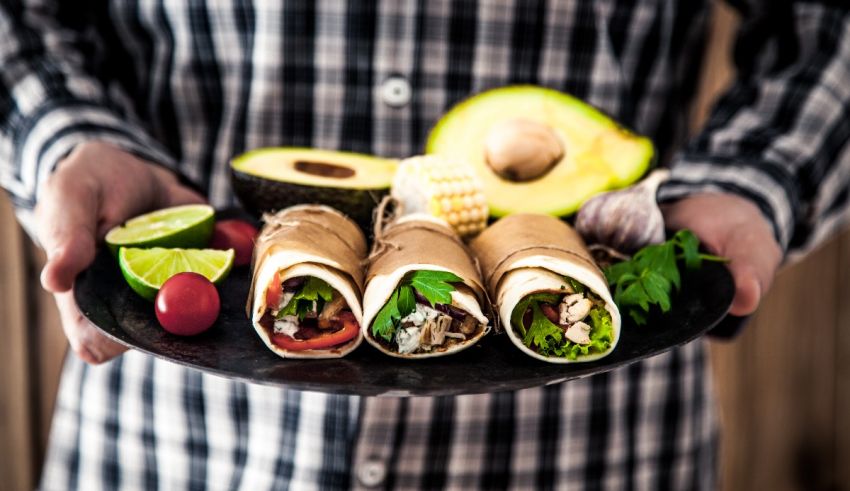 A man is holding a plate full of wraps and vegetables.
