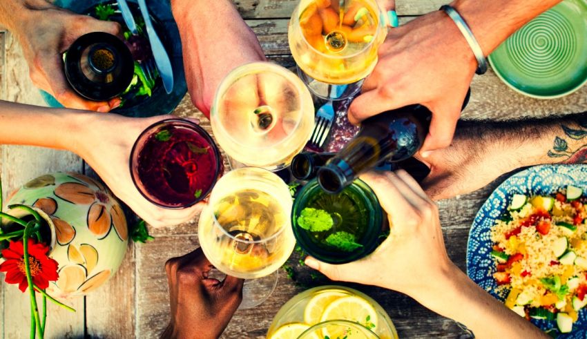 A group of people toasting with drinks and food on a wooden table.