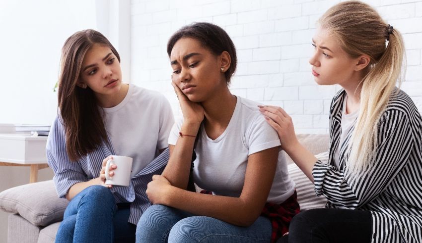 Three young women sitting on a couch talking to each other.