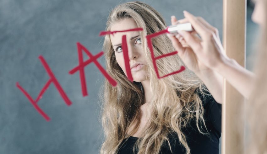 A woman writing the word hate on a mirror.
