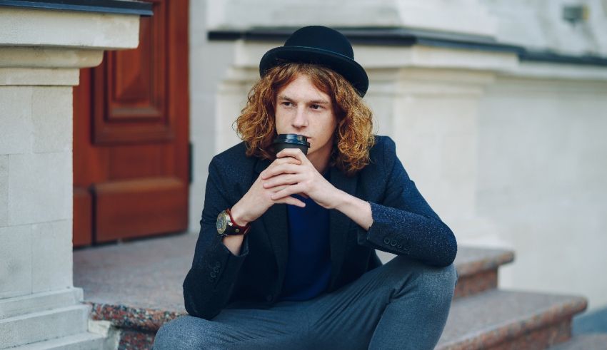 A young man with curly hair sitting on the steps of a building.