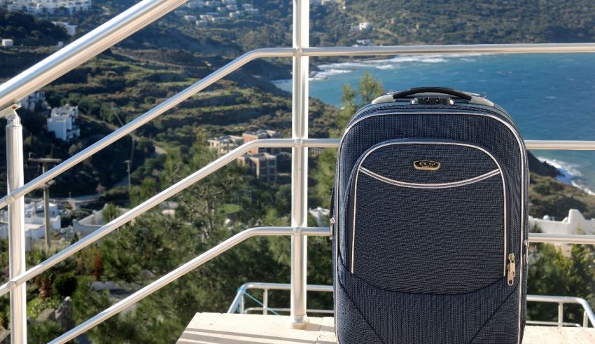 A blue suitcase sits on a railing overlooking the ocean.
