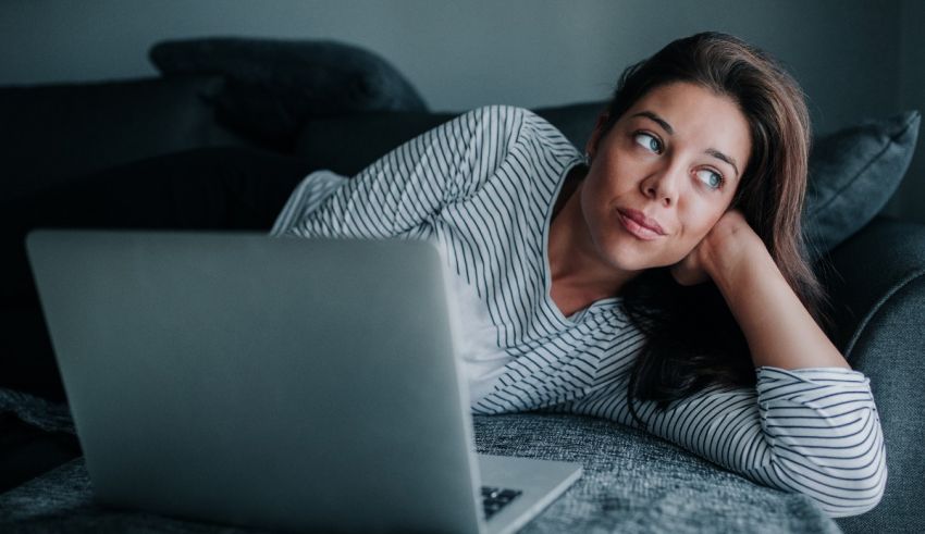 A woman laying on a couch looking at her laptop.
