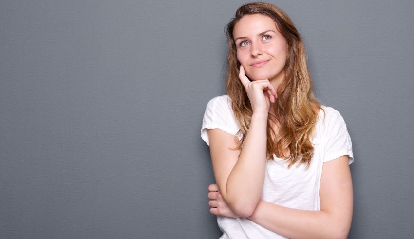 A young woman leaning against a gray wall with her hand on her chin.