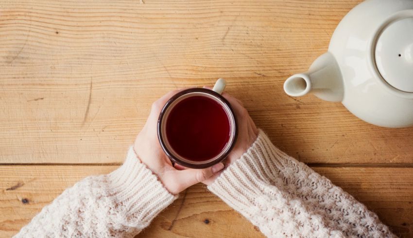 A woman's hands holding a cup of tea on a wooden table.