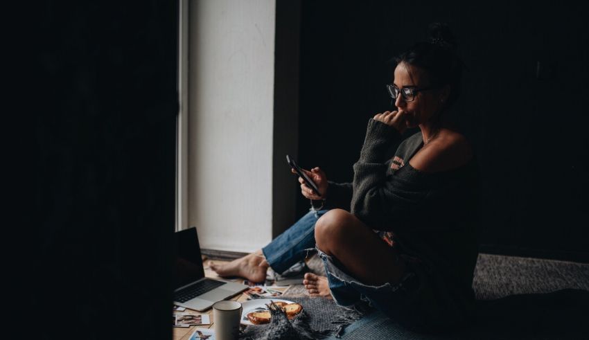 A woman sitting on the floor looking at her phone.